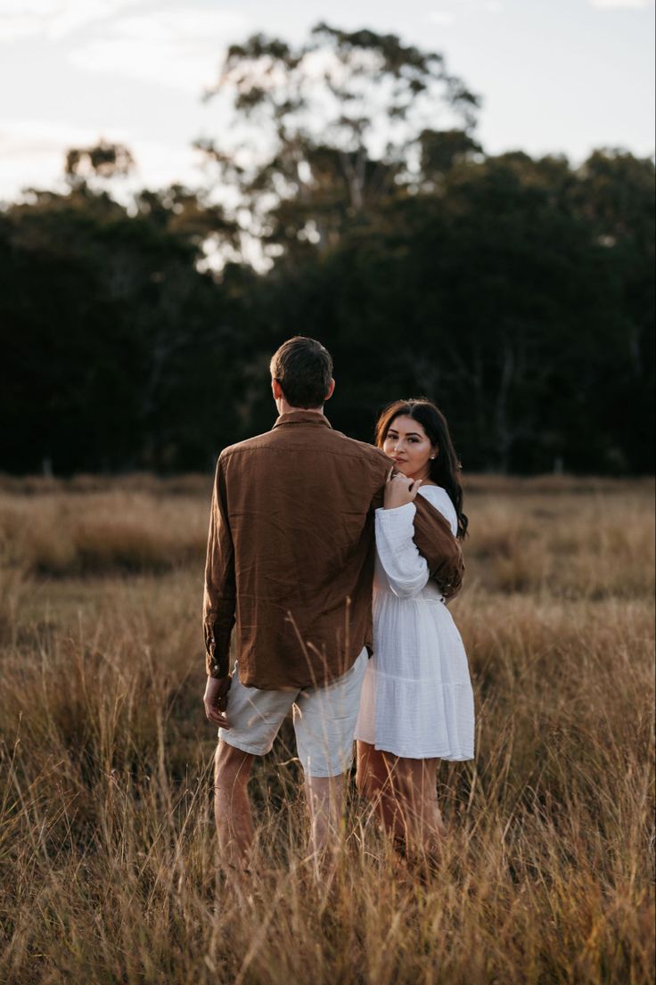 a man and woman are standing in the tall grass looking into each other's eyes