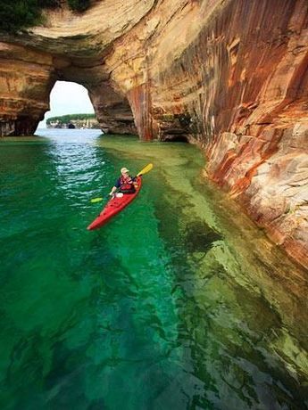 a person in a kayak paddling through the water near a large rock formation