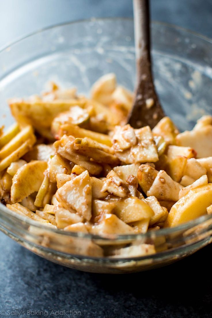 a glass bowl filled with food sitting on top of a black counter next to a wooden spoon