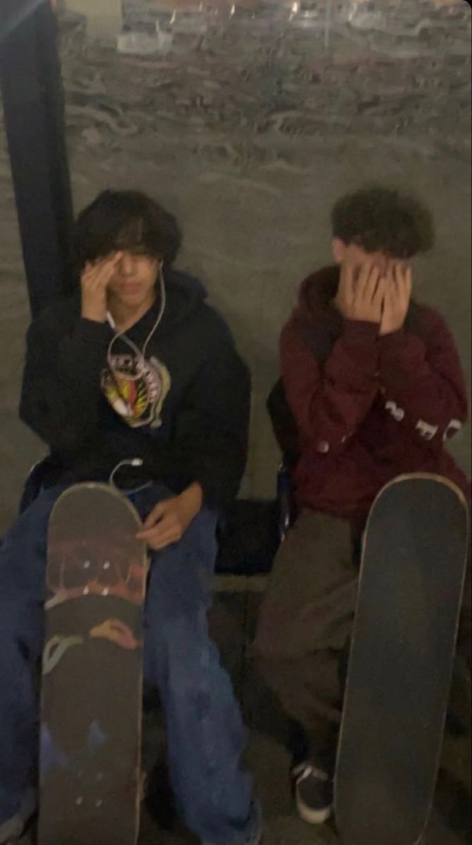 two young men sitting next to each other with skateboards on their feet and covering their faces