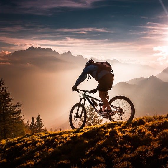 black and white photograph of a mountain biker on top of a hill with mountains in the background