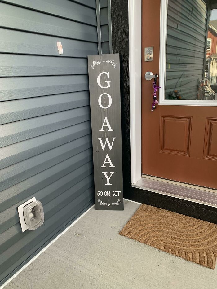 a sign that says go away on the front porch next to a door with a welcome mat