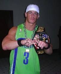 a man in a green shirt holding up a wrestling belt and wearing a white hat