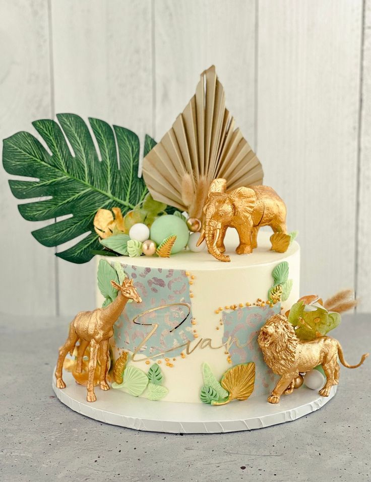 a cake decorated with animals and leaves on top of a white table next to a wooden wall