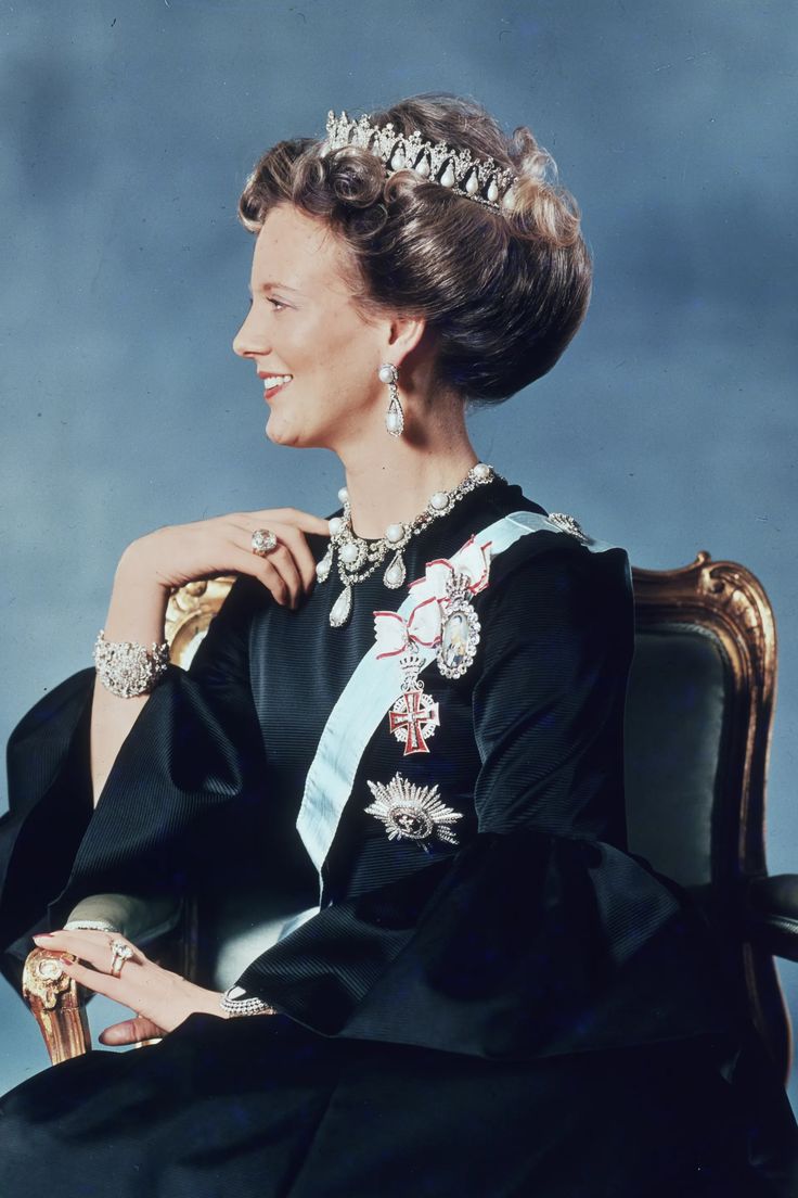 an old photo of a woman in a black dress and tiara sitting on a chair