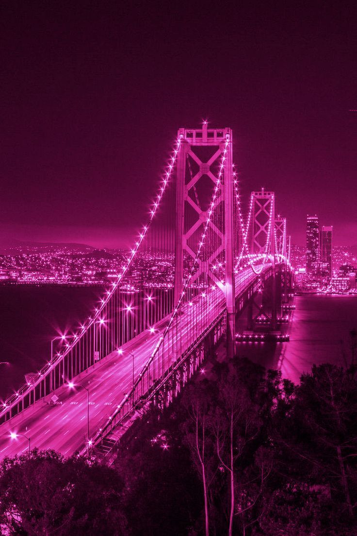 the bay bridge is lit up at night with lights on and cars driving over it