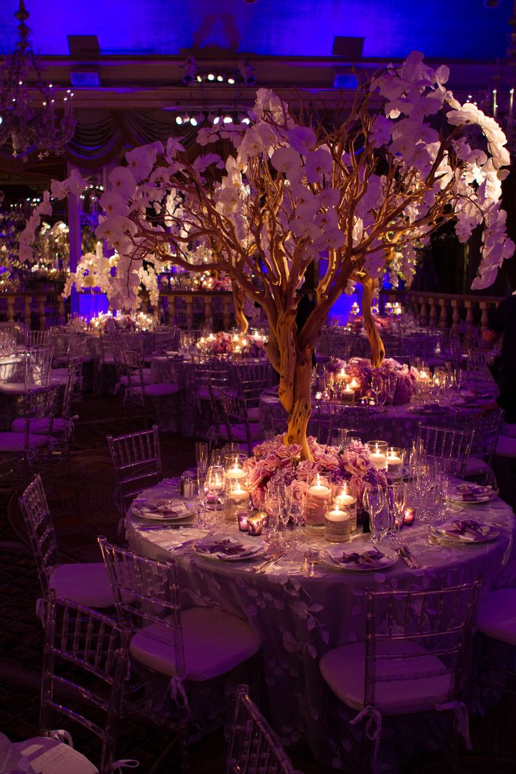 the centerpieces are decorated with flowers, candles and trees in purple lighting for an elegant wedding reception