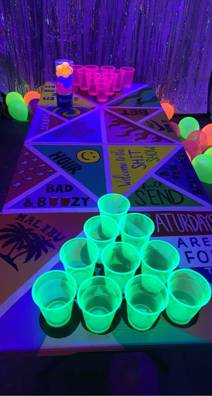 neon glow cups are sitting on a table in the middle of a room with purple and green lights