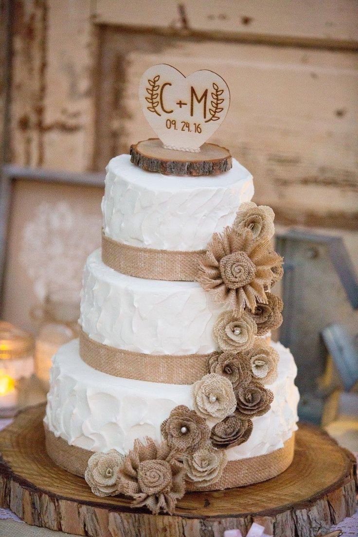 a three tiered wedding cake with burlap flowers and ribbon on the top