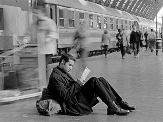 a man sitting on the ground reading a book in front of a train at a station