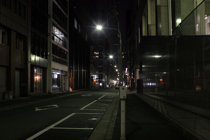 an empty city street at night with no people or cars on the road and buildings in the background