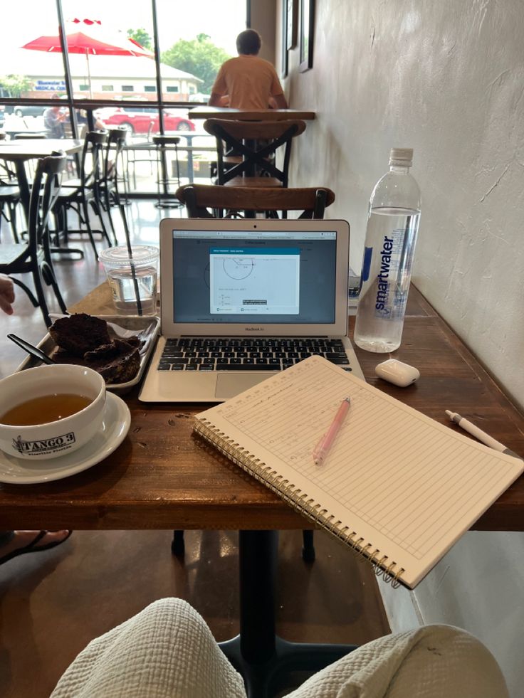 a laptop computer sitting on top of a wooden table next to a cup of coffee