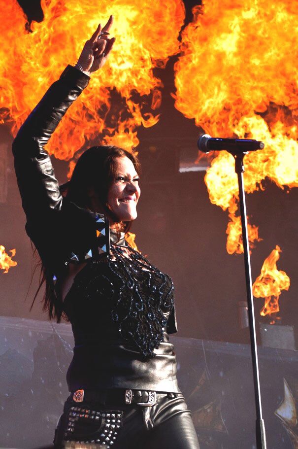 a woman with her arms in the air while standing next to a microphone on fire