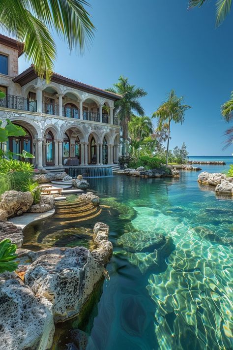 a large house sitting on top of a lush green hillside next to the ocean with clear blue water