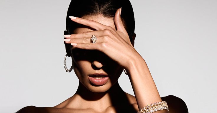 a woman with her hands on her face and wearing jewelry around her neck, posing for the camera