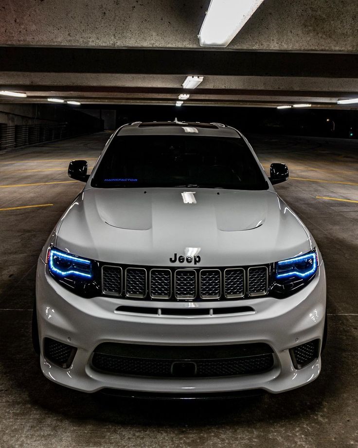the front end of a white jeep parked in a parking garage with its lights on