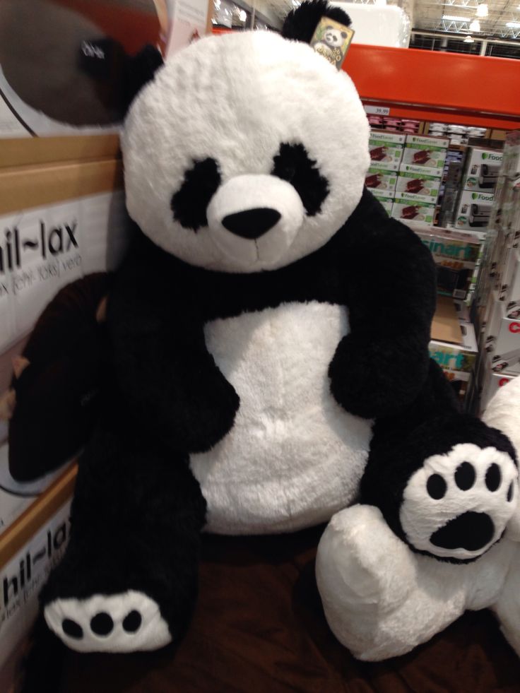 a large stuffed panda bear sitting on top of a wooden floor next to other stuffed animals