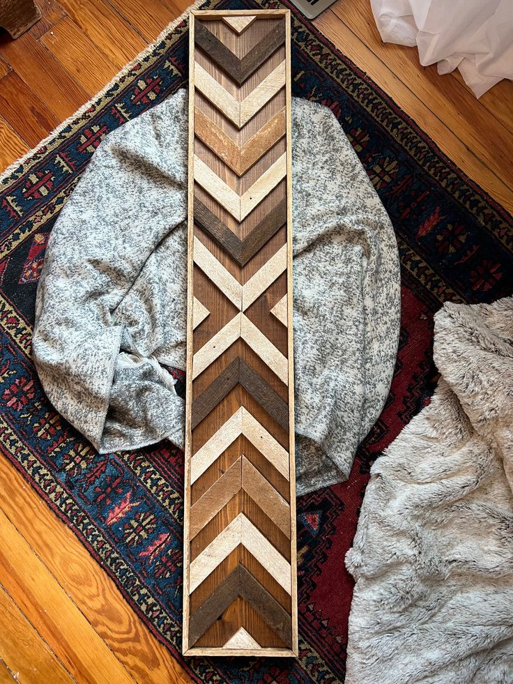 a wooden chevron pattern sitting on top of a rug next to a pile of blankets