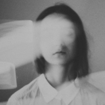 black and white photograph of a woman's face in front of a bed with sheets