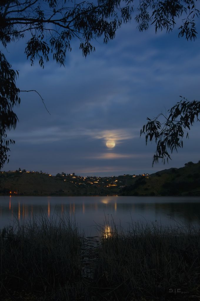 the full moon is setting over a lake