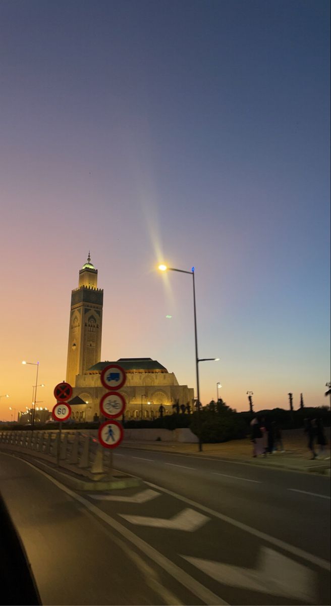 a clock tower is in the background as people walk by at sunset or dawn on a city street