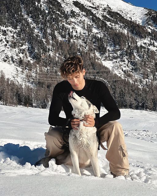 a young man sitting in the snow with his white and black husky dog next to him