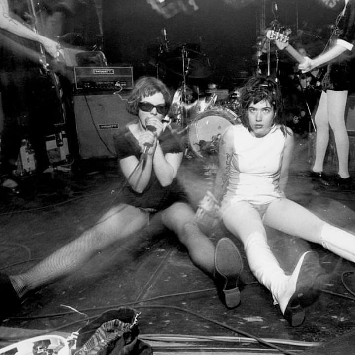 two women sitting on the floor with their legs crossed in front of them, one holding a microphone