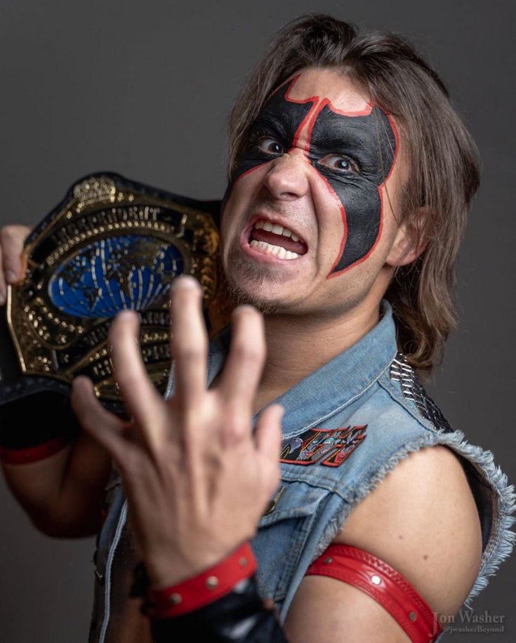 a man with his face painted like a wrestler holding up a wrestling ring and making the peace sign