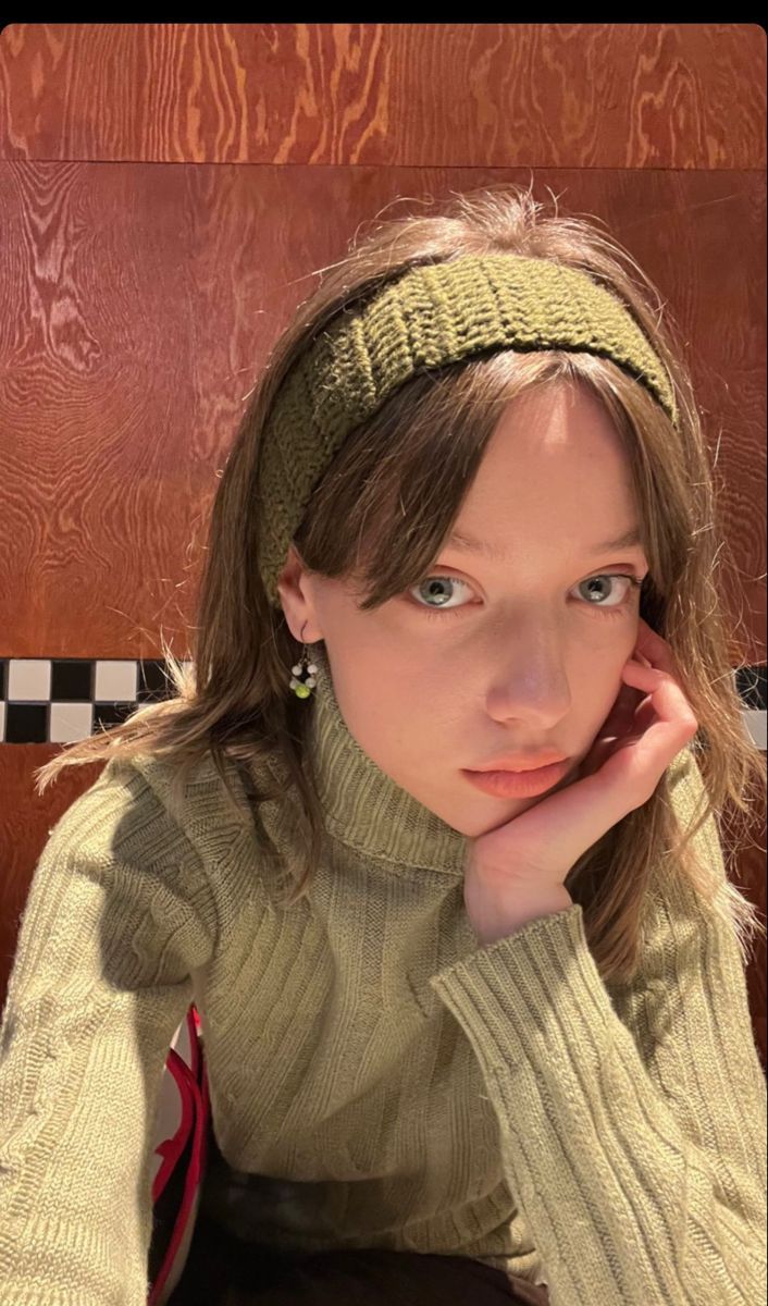 a woman sitting in front of a wooden wall with her hand on her chin and looking at the camera