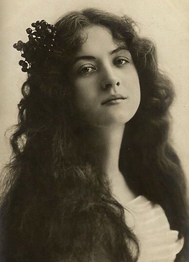 an old black and white photo of a woman with long hair wearing a flower in her hair