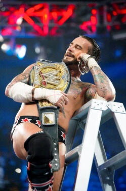 a man with tattoos on his arm and knee standing next to a ladder holding a wrestling belt