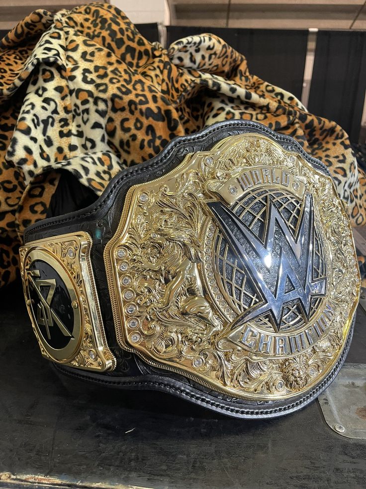 a gold and black wrestling belt sitting on top of a leopard print cloth covered bag