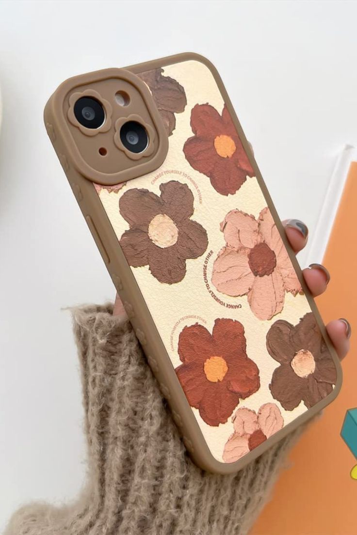 a woman is holding her phone case with flowers on the front and back, while she's wearing a brown sweater