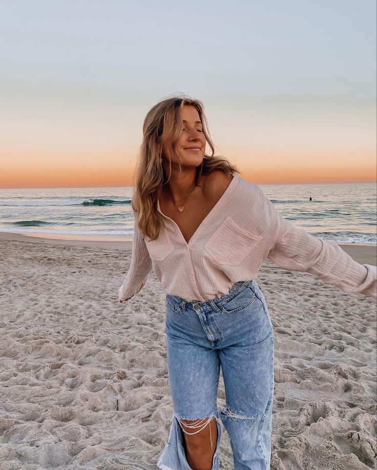 a woman standing on top of a sandy beach next to the ocean with her arms outstretched