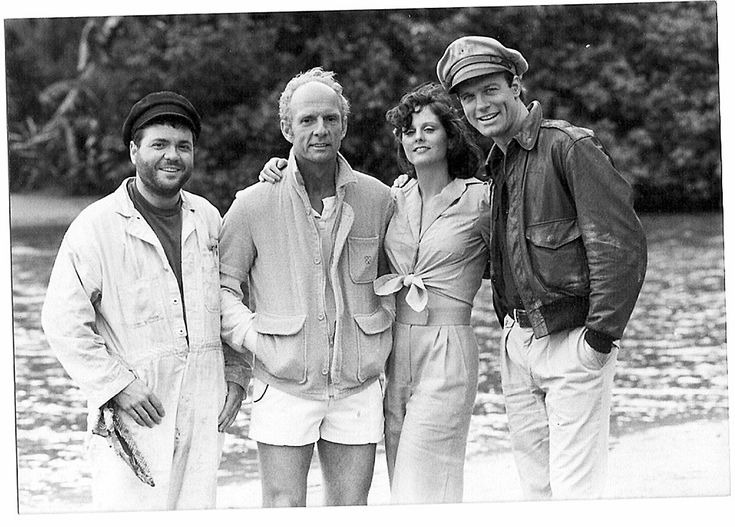 an old black and white photo of four people standing next to each other in front of water