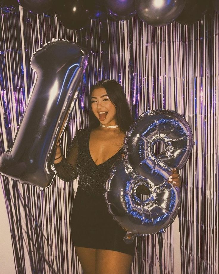 a woman is holding balloons and posing for a photo in front of some foil streamers