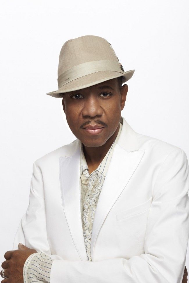 a man in a white suit and hat with his arms crossed, looking at the camera