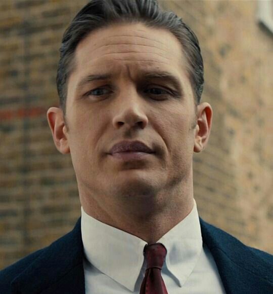 a man wearing a suit and tie standing in front of a brick building with his eyes closed