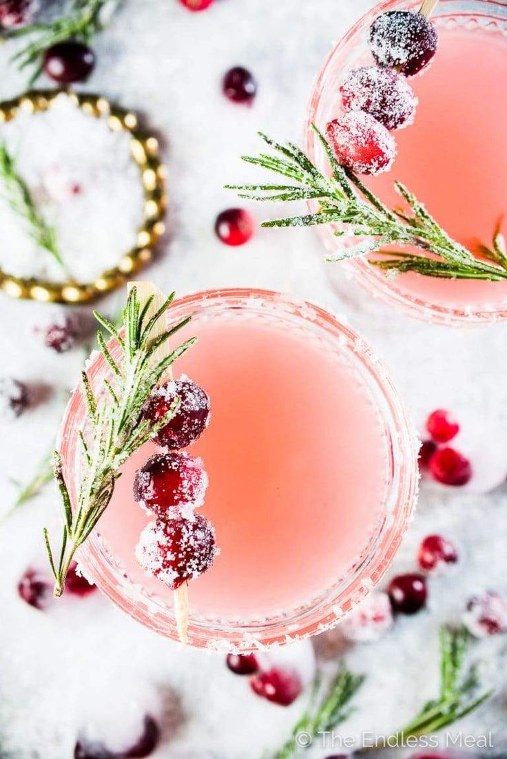 two glasses filled with cranberry and rosemary cocktails on top of snow covered ground