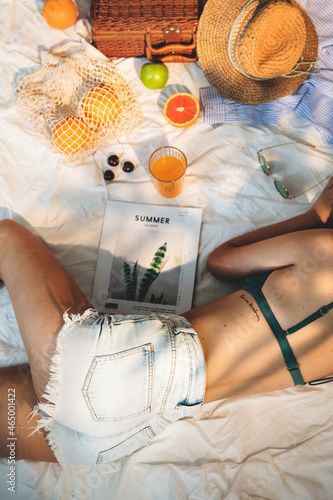 a woman laying on top of a bed next to an orange juice and straw hat