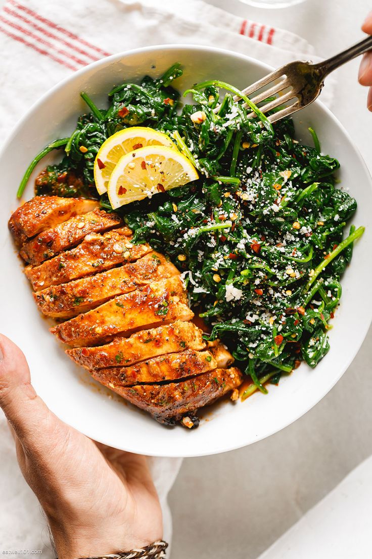 a person holding a plate with meat, greens and lemon wedges on the side