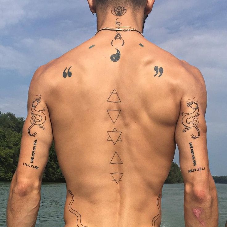 a man with tattoos on his back standing next to the water