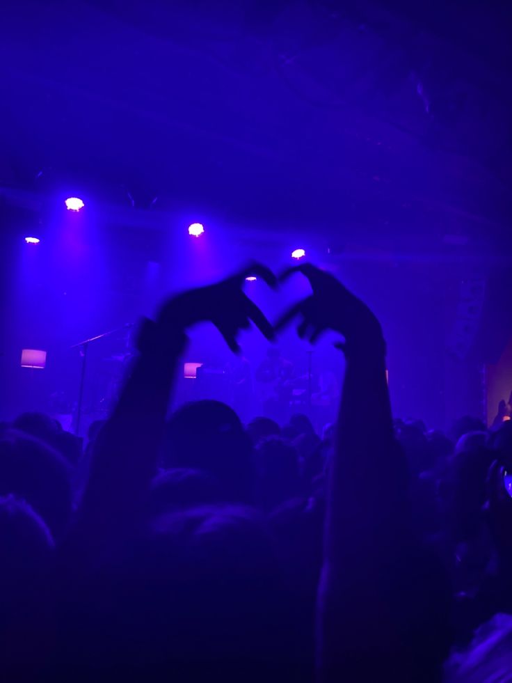two hands making a heart with their fingers in front of a crowd at a concert