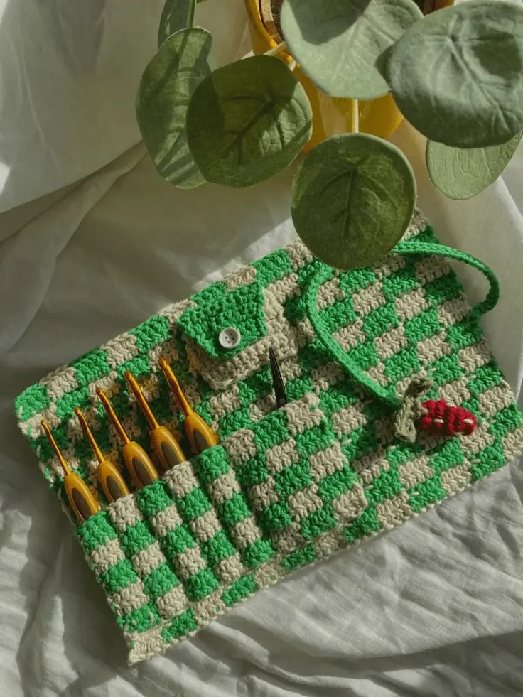 a crocheted green and white purse sitting on top of a bed next to a potted plant