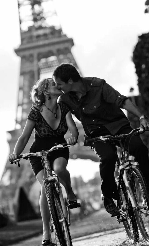 a man and woman kissing while riding bikes in front of the eiffel tower