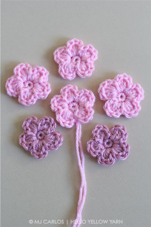 four crocheted flowers on a white surface with a pink string in the middle