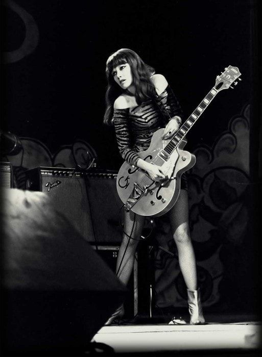 a woman with long hair playing an electric guitar in black and white, while standing on a stage