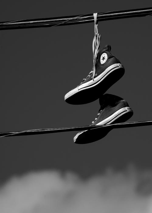 black and white photograph of shoes hanging on power lines with clouds in the back ground