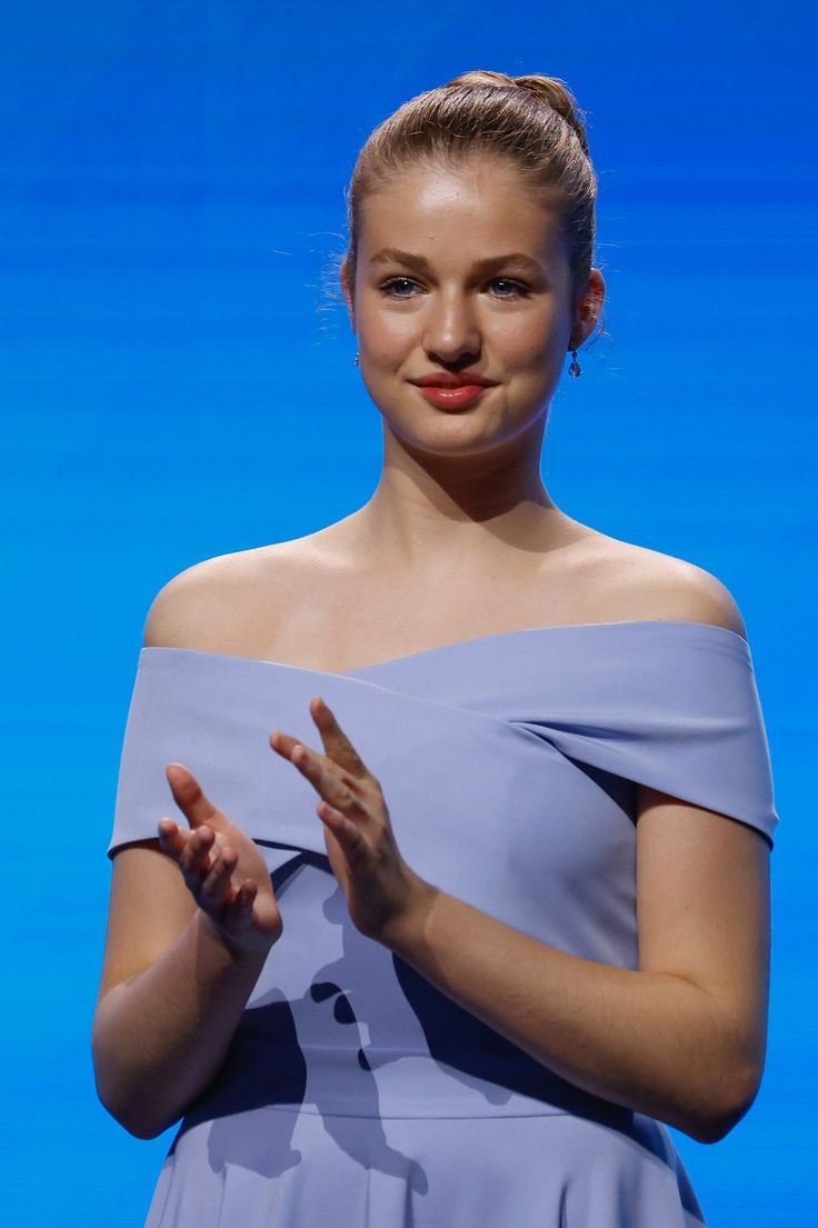 a woman standing in front of a blue background with her hands folded out to the side