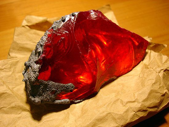 a piece of red glass sitting on top of a piece of brown paper next to a wooden table